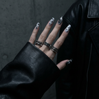 Hand model wearing Anti-Valentine handmade press-on nails in a long coffin shape. The nails feature black and silver magnetic cat-eye gel with hand-painted 'Boy Bye' lettering and heart motifs. Styled with a black leather jacket and chunky silver rings for a grunge, goth, and edgy streetwear aesthetic.