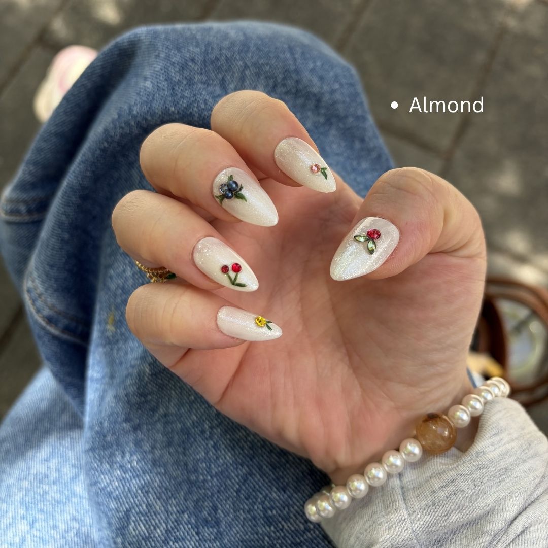 Handmade press-on nails featuring hand-painted cherries and blueberries, accented with sparkling Swarovski charms on a shimmering white base.