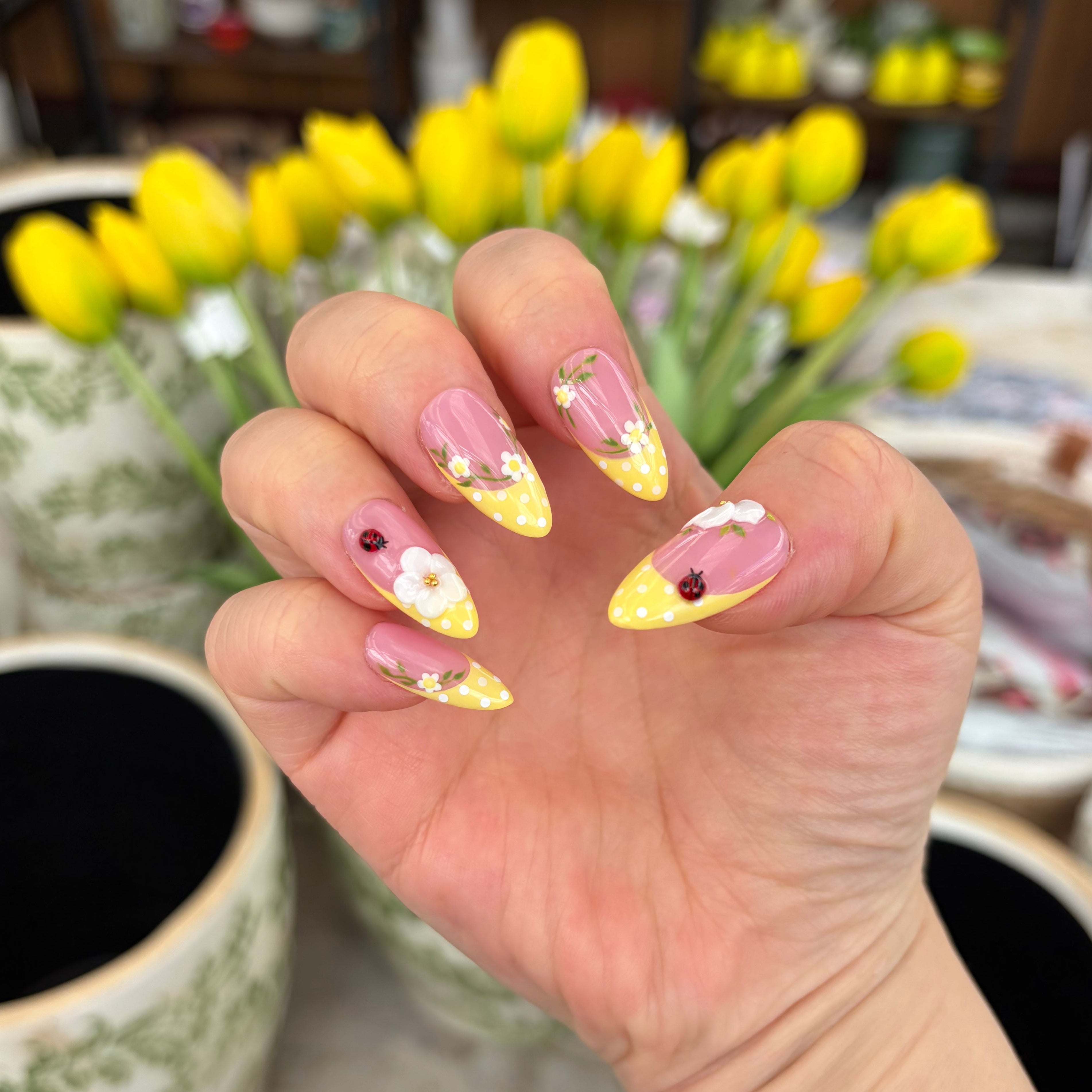 Vibrant handmade press-on nails from the Bloom & Glory collection featuring 3D white garden flowers, ladybug and yellow polka dots, and 3D ladybug accents.
