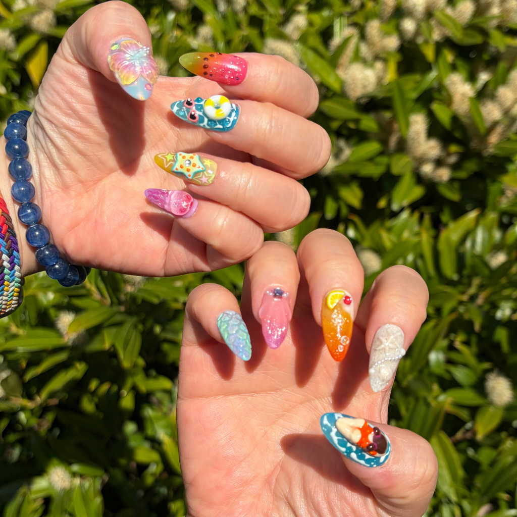 a real person wearing press-on nails. Bring the ocean to your fingertips with "Ocean Dip"—a maximalist press-on nail set featuring 3D waves, sea life, swimmers, and beach icons. These handmade, reusable gel nails are the ultimate accessory for your beach vacation. Custom-fit and vibrant