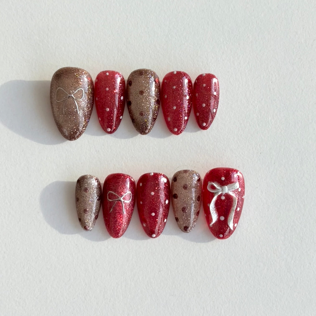 Handmade press-on nails in alternating ruby red and champagne glitter with white bows and polka dot accents.