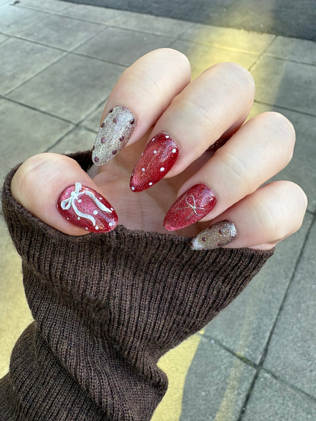 Hand model wearing Champagne & Crimson Couture nails with a cozy brown sweater showcasing a festive, elegant manicure.