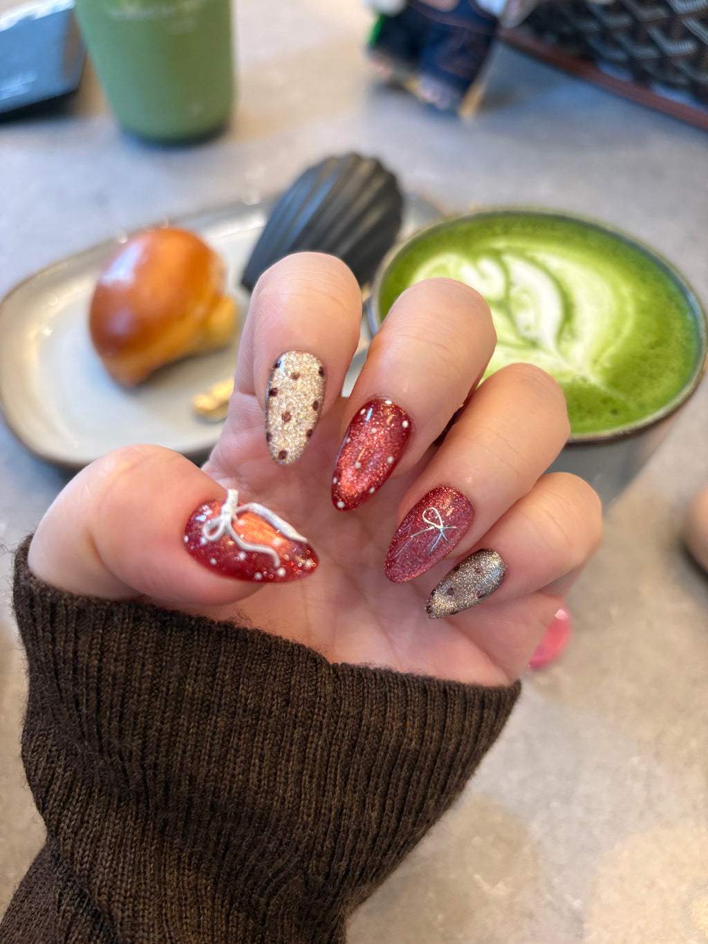 Hand with glittery nail polish holding a plate with matcha and pastry