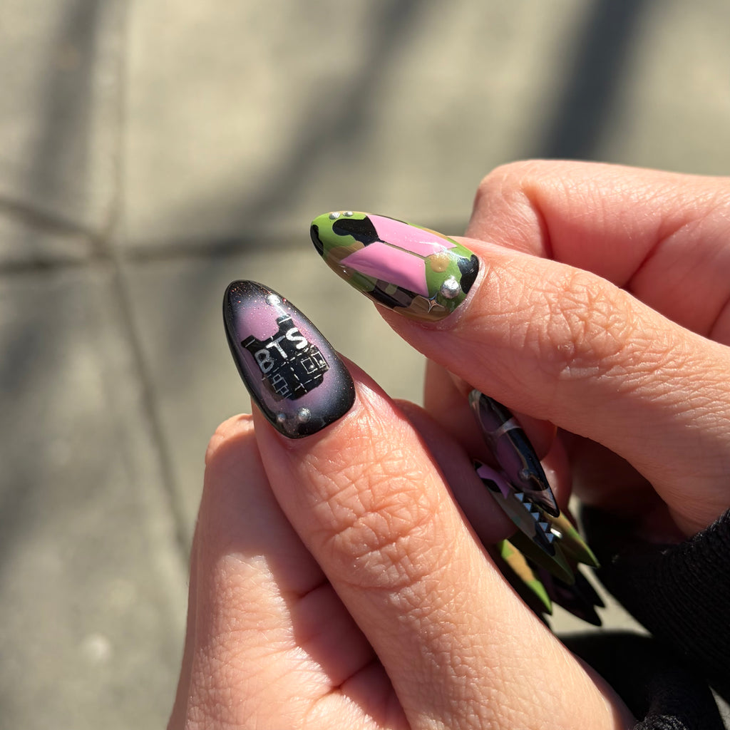 Close-up of a hand with colorful nail art, including a design with 'BTS' on a purple background.