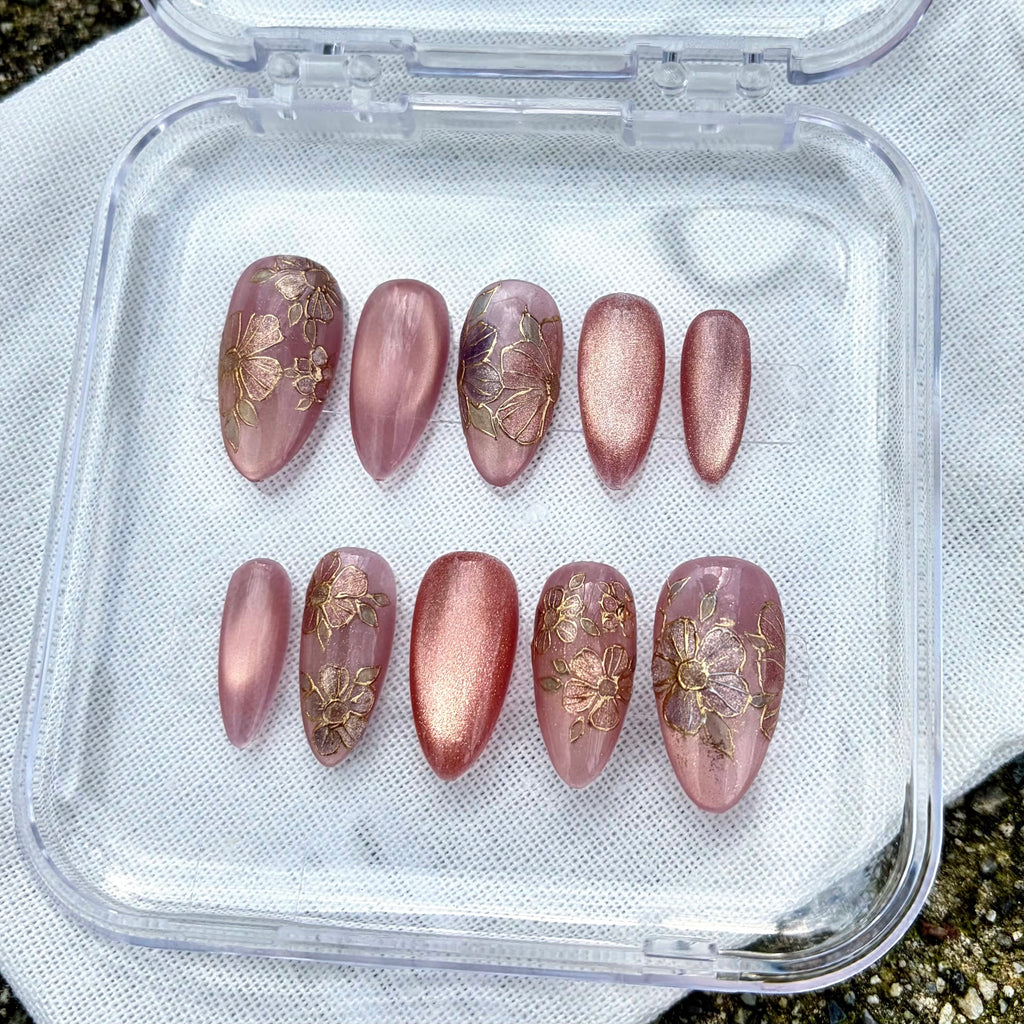 Handmade press-on nails with a soft pink and deep purple ombre gradient, featuring hand-painted flowers and cat-eye gold glitter.