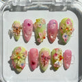 Close-up of the intricate green vine artwork and 3D textured flowers on a soft yellow spring press-on nail.