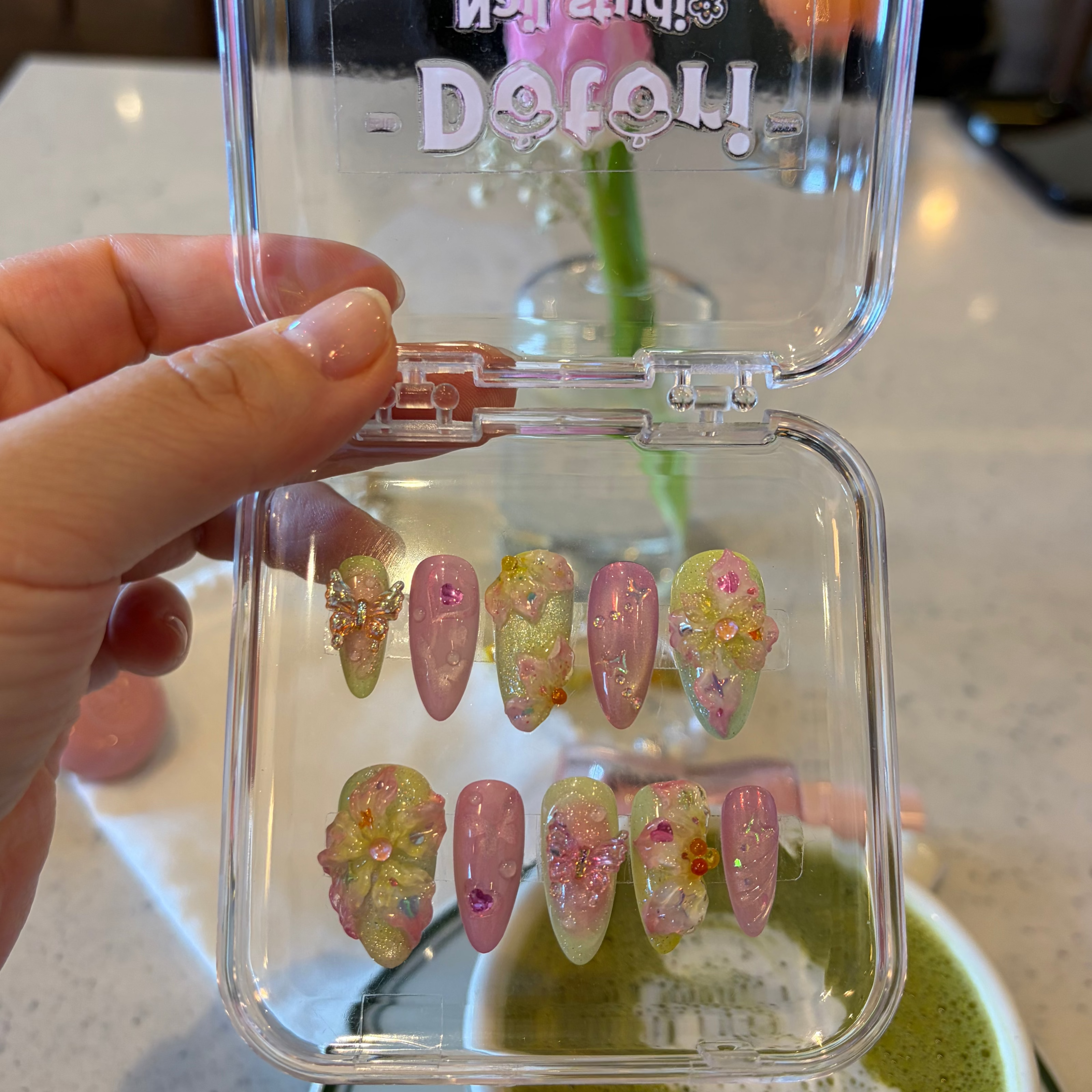 Close-up of the intricate green vine artwork and 3D textured flowers and butterfly on a soft yellow spring press-on nail. 