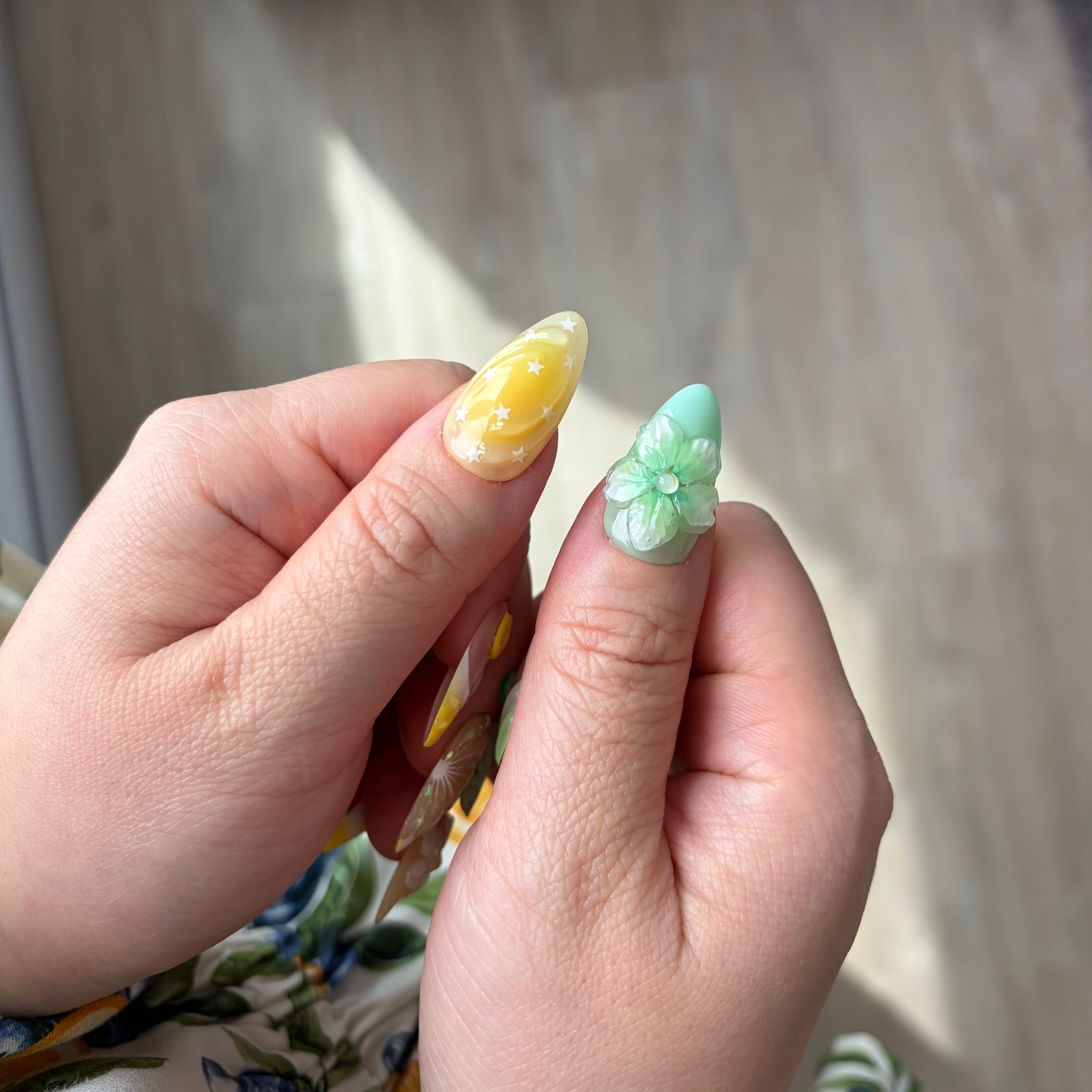 Close-up of a hand with decorative nail art holding two nail samples.