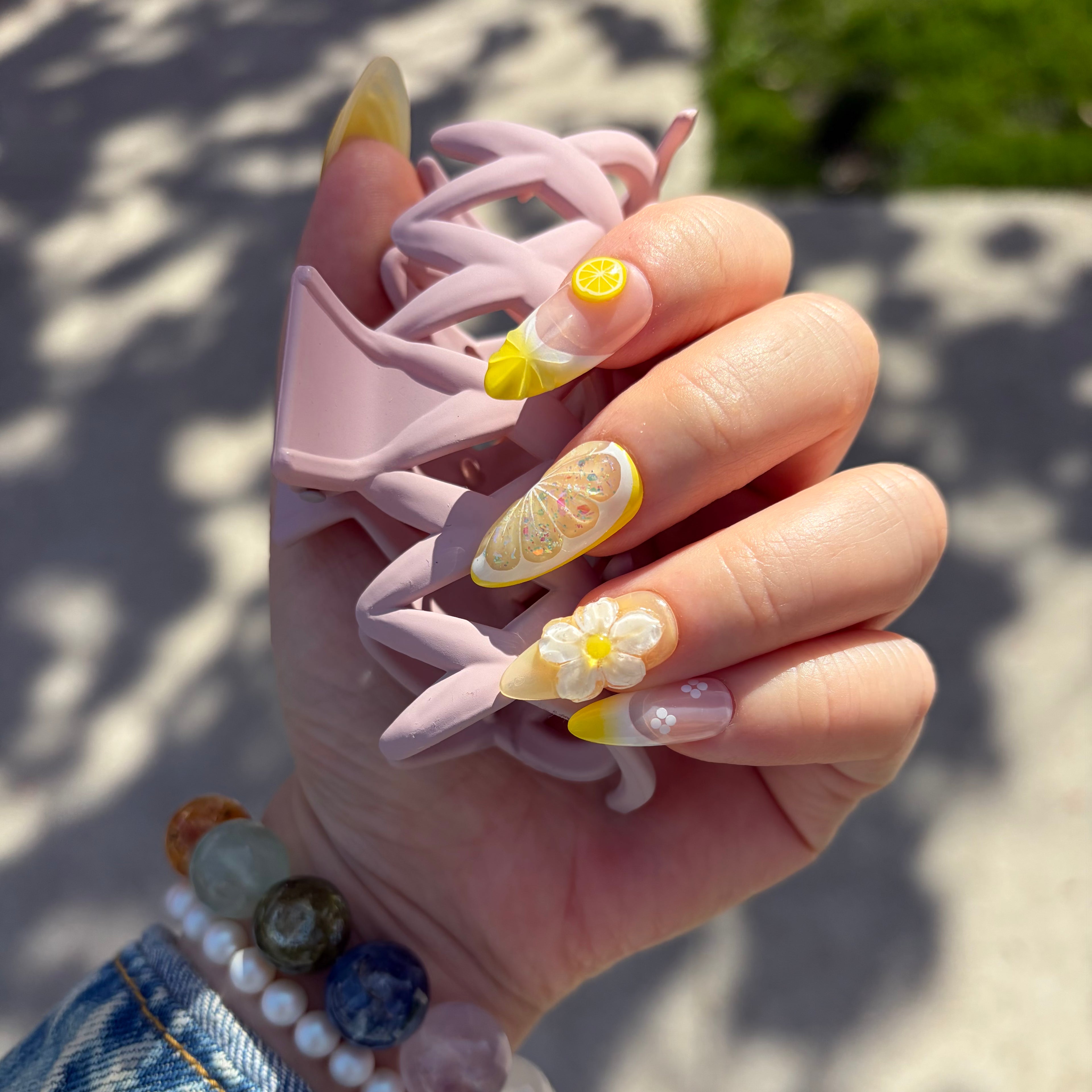 Close-up of the realistic citrus fruit slice charms and 3D sculpted floral details on a vibrant summer nail set.