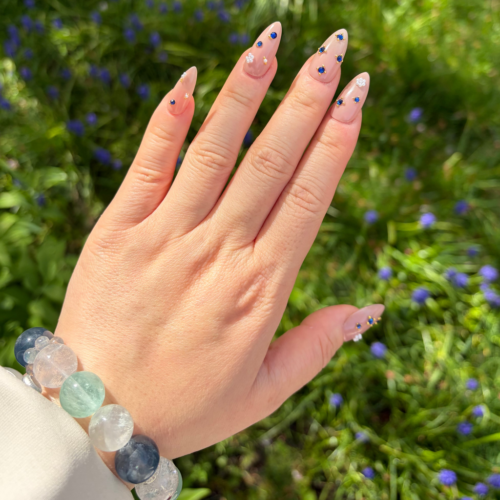 Handmade luxury press-on nails with Swarovski sapphire gemstones and white pearl flower accents on a soft nude gel base.