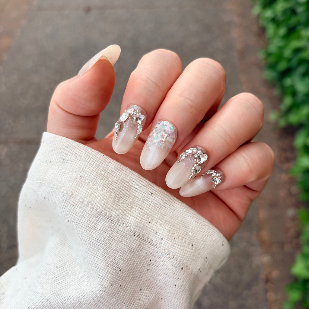 Handmade luxury press-on nails with Swarovski crystal clusters and iridescent star glitters on a shimmering milky-nude gel base.