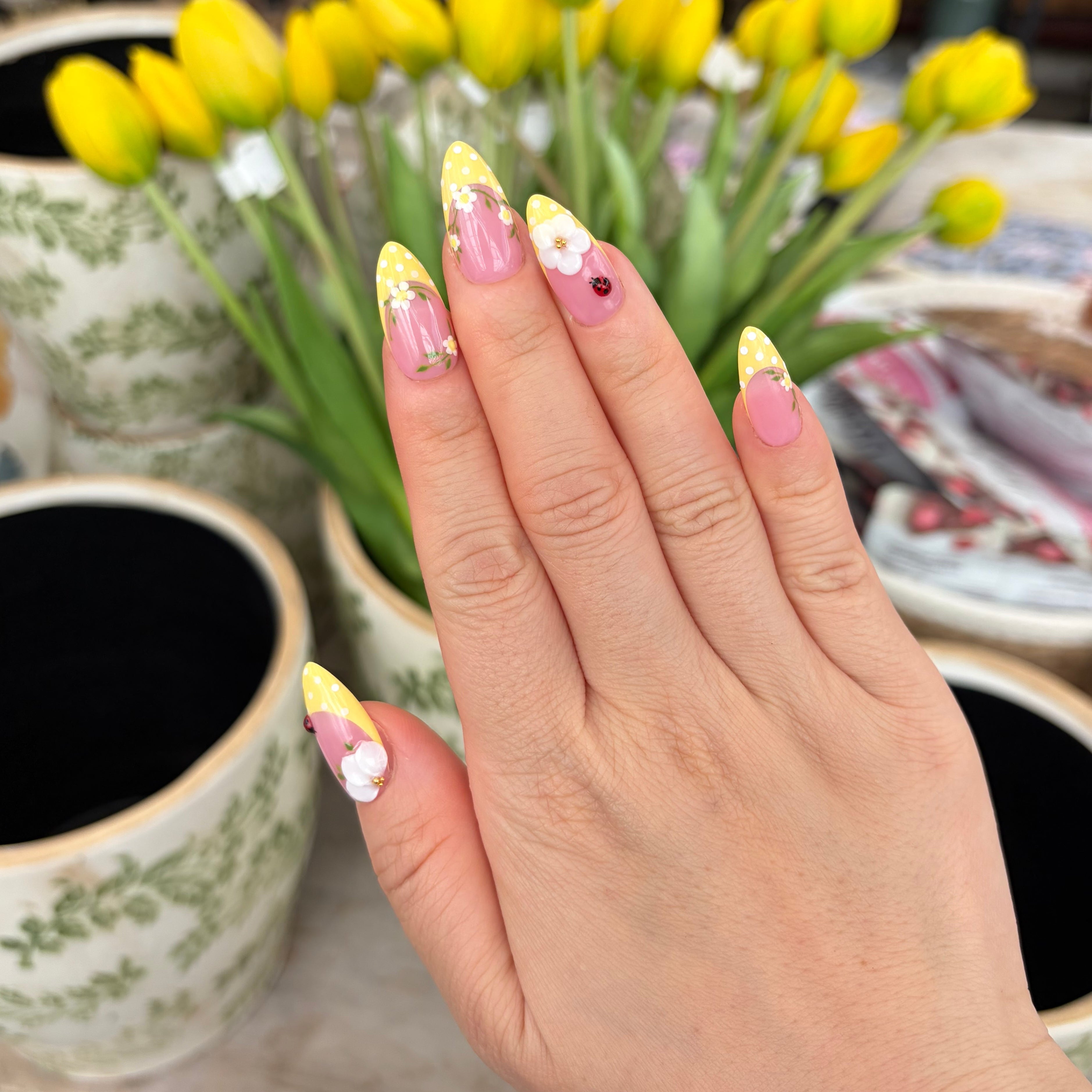 Vibrant handmade press-on nails from the Bloom & Glory collection featuring 3D white garden flowers, yellow polka dots, and 3D ladybug accents.
