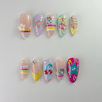 Handmade Y2K collection press-on nails featuring 3D fruit and flower charms, colorful rainbow stripes, teal stars, and crystal rhinestone designs on a multi-colored pastel