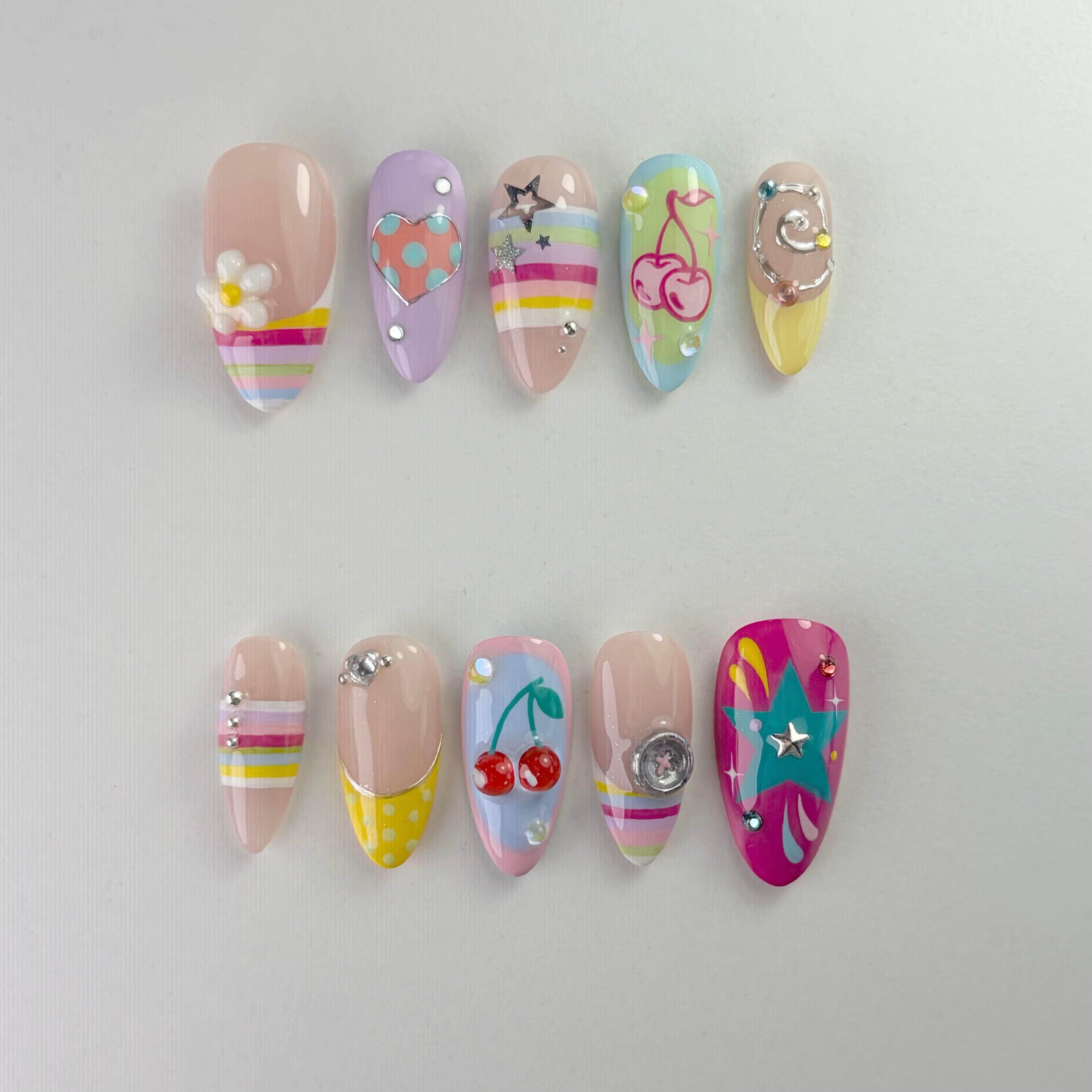 Handmade Y2K collection press-on nails featuring 3D fruit and flower charms, colorful rainbow stripes, teal stars, and crystal rhinestone designs on a multi-colored pastel