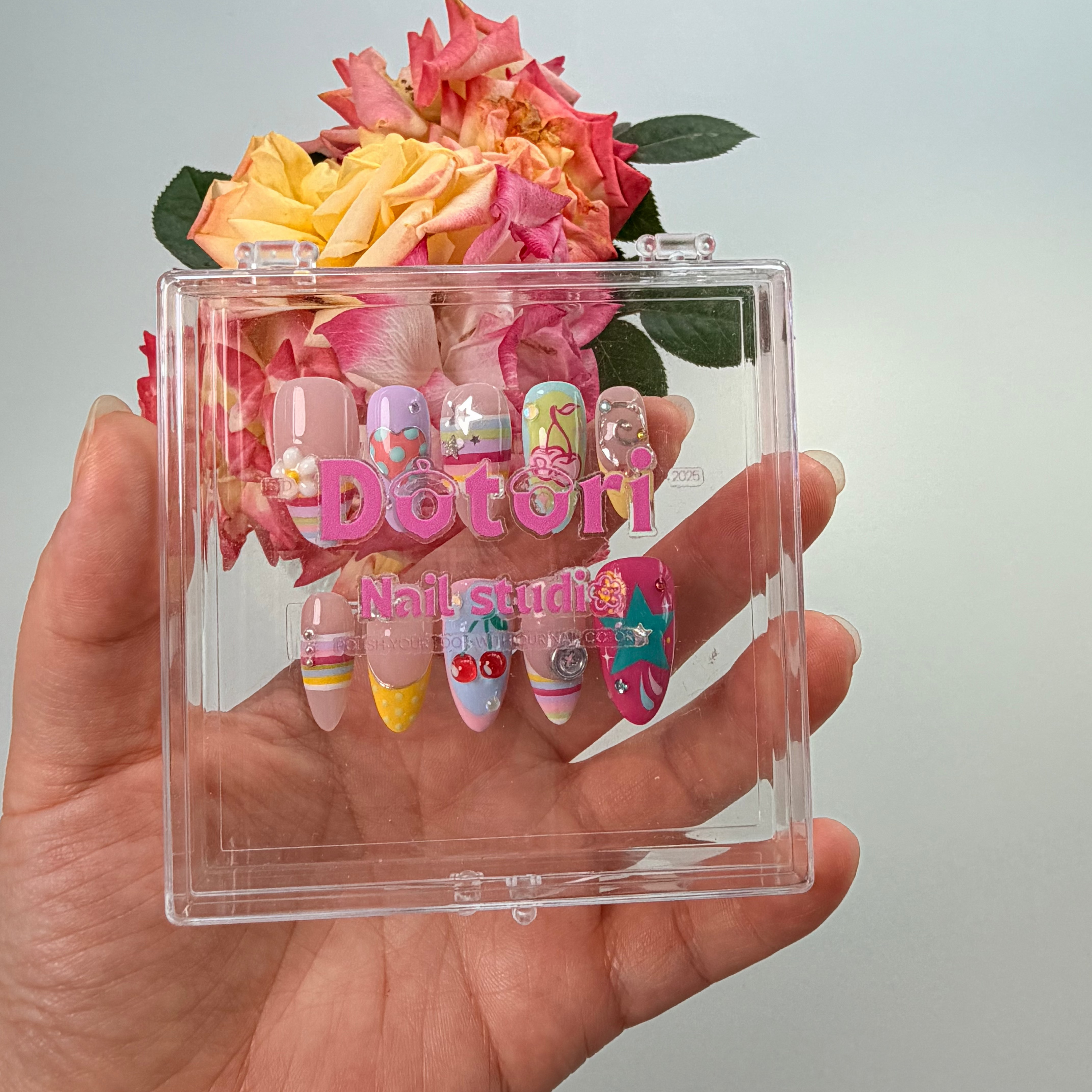 Handmade Y2K collection press-on nails featuring 3D fruit and flower charms, colorful rainbow stripes, teal stars, and crystal rhinestone designs on a multi-colored pastel